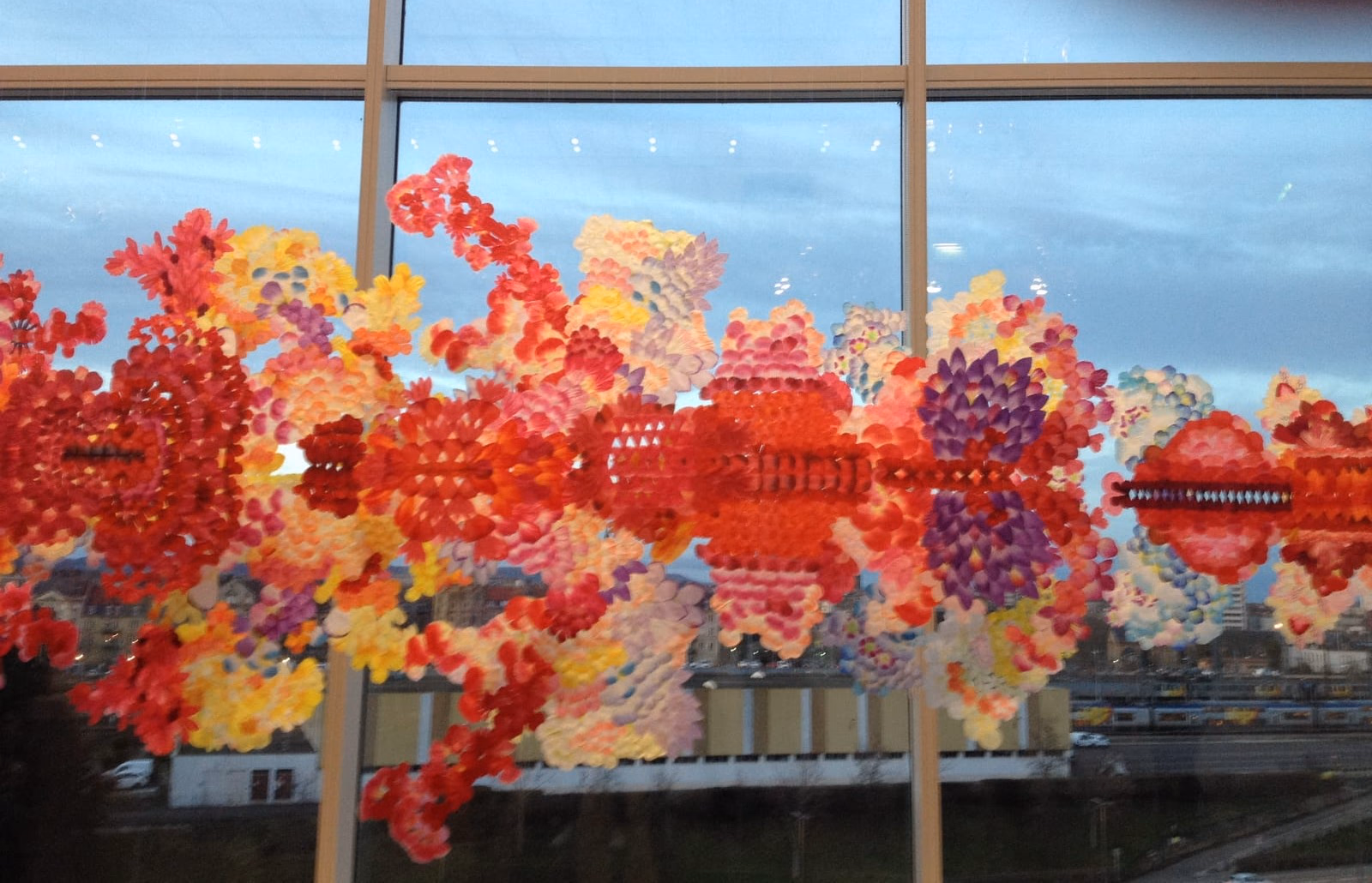 Des fleurs découpées dans du papier de couleur, collées sur une grande baie vitrée à contre-jour.
